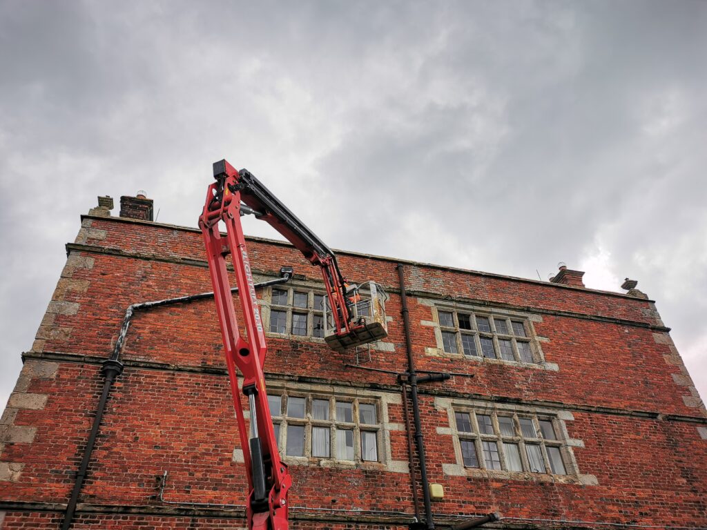 The use of a cherry picker highlights the significant height of the windows, emphasizing the impressive scale of the structure and the dedication required for their repair.