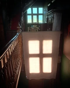 A cross of the crucifixion projected onto a cloth as the sun sets on Good Friday, this is happening in a manor house interior of a gallery space