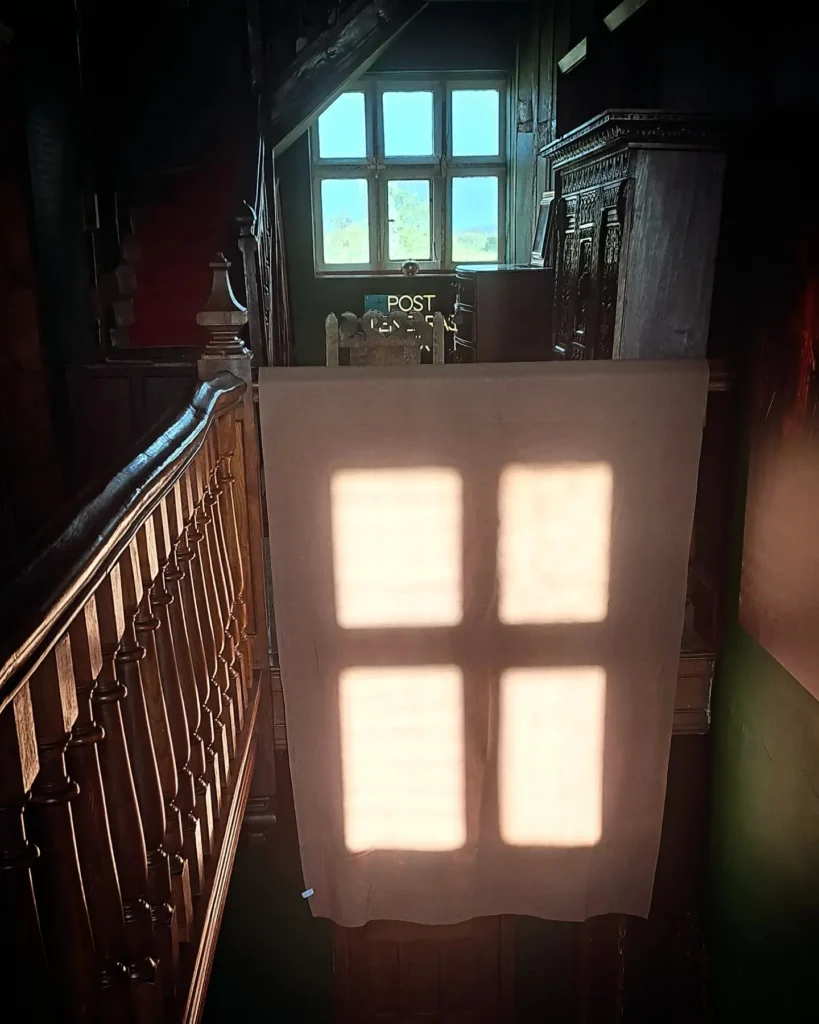 A cross of the crucifixion projected onto a cloth as the sun sets on Good Friday, this is happening in a manor house interior of a gallery space