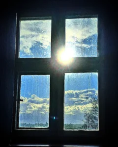 Golden Hour Sun backlights a cross of stone mullions on a window casement. outisde it is sunny, inside it appears dark