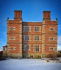 Soulton Hall in the snow- we see a reb brick cube of a Tudoe building