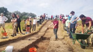 Archaeologists and the public are looking at a trench in a mound, explaining a lost castle feature.