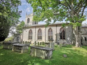 A church yard with trees, the stone church beyond