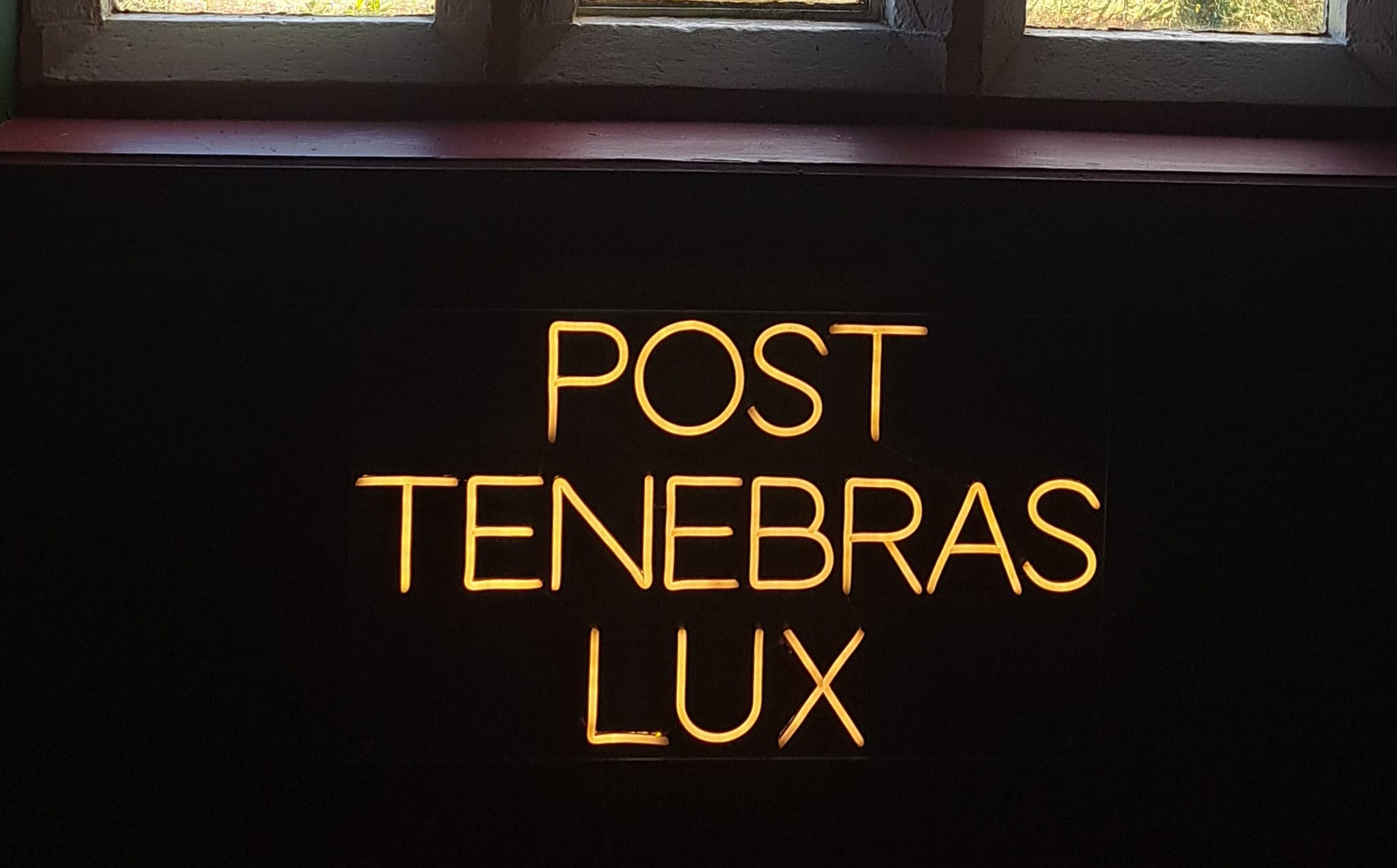 A neon artwork in warm white with the latin words POST TENEBRAS LUX on it