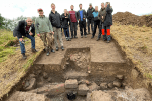 Archaeologists stand by a trench exposing a timber bridge and stone footings on Soulton Mound