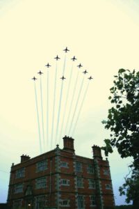 a V formation of RAF red arrows fly past Soulton Hall leaving a smoke trails