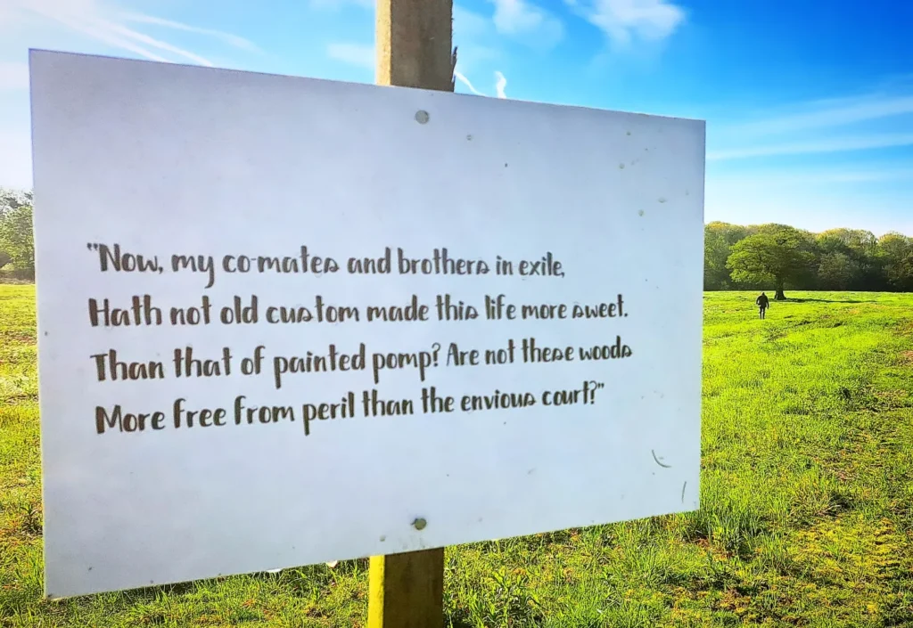 A sign with an AS YOU LIKE IT quotation in the Soulton landscape: Now, my co-mates and brothers in exile, Hath not old custom made this life more sweet Than that of painted pomp? Are not these woods More free from peril than the envious court?